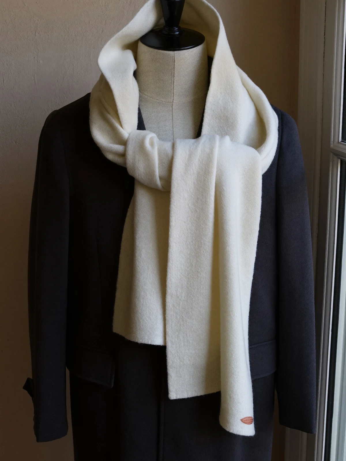 Écharpe de laine ivoire drapée sur un manteau de laine anthracite